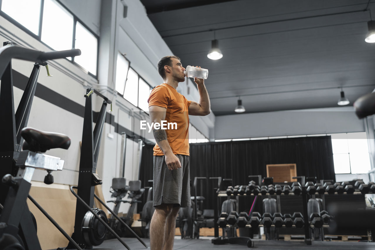 Mid adult man drinking water while standing in gym