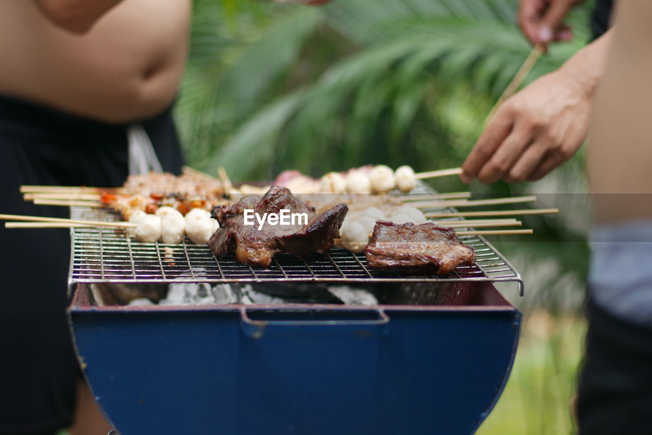 Midsection of man preparing meat on barbecue grill