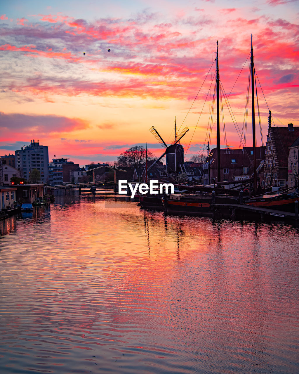 SAILBOATS MOORED IN HARBOR AT SUNSET