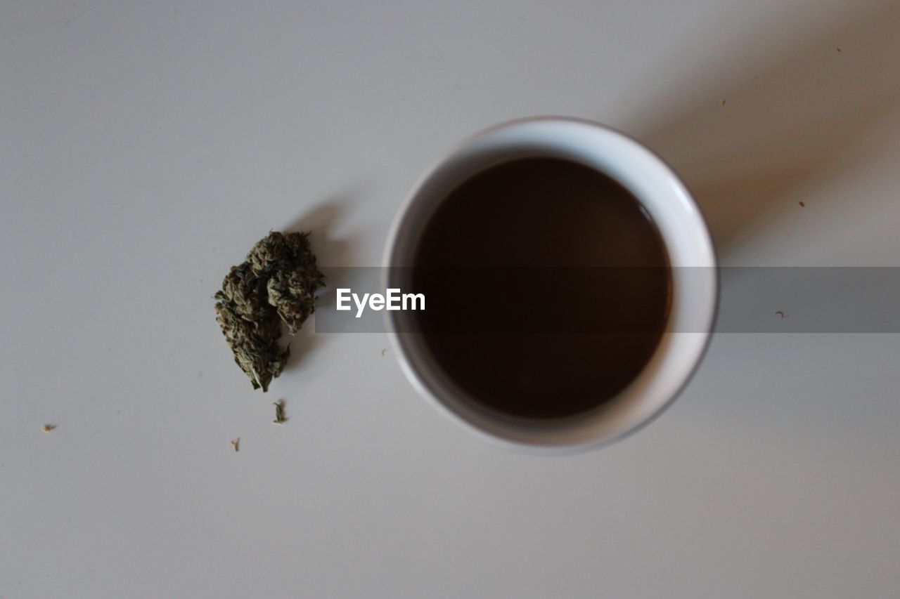 Directly above shot of tea cup with marijuana on white background