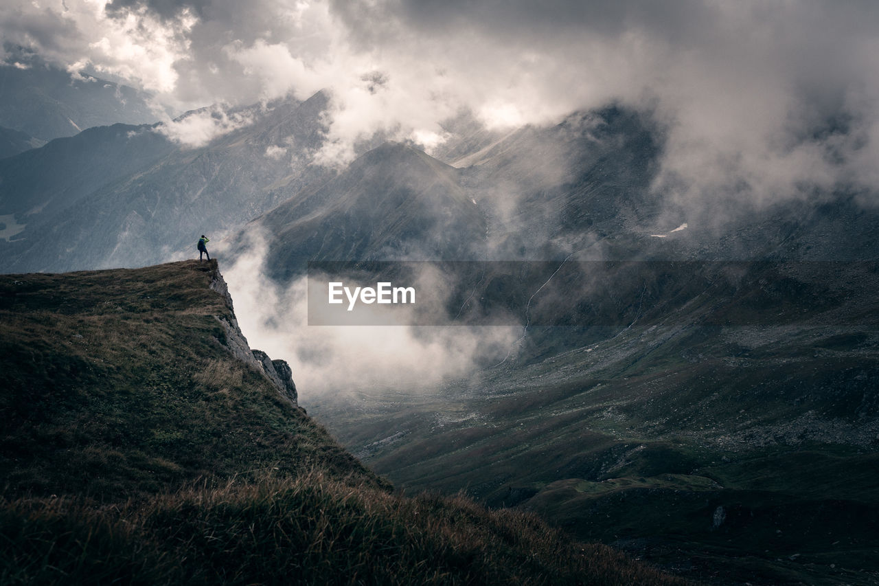 Distant view of man standing on mountain against sky