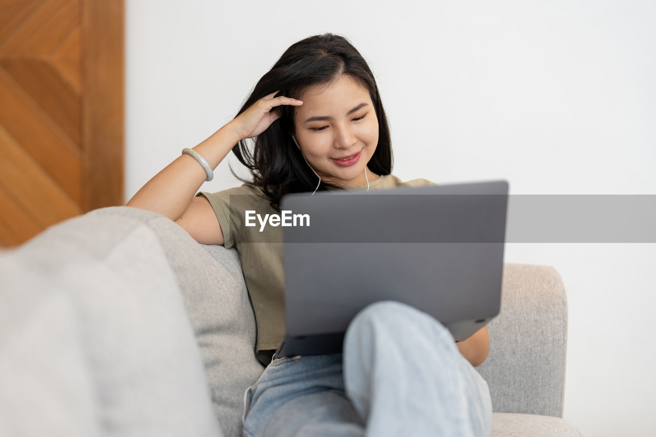 portrait of woman using laptop while sitting on sofa at home