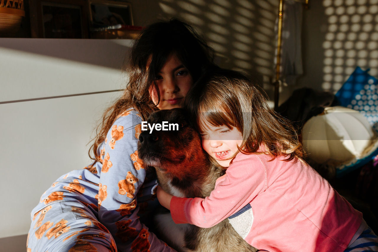 Children hugging their dog sitting altogether in the bed