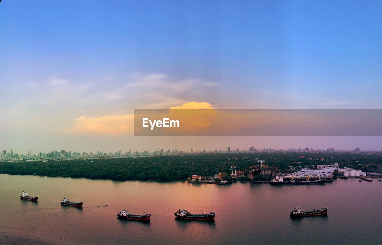 Sunset over chao phraya river with boats and bangkok cityscape in background