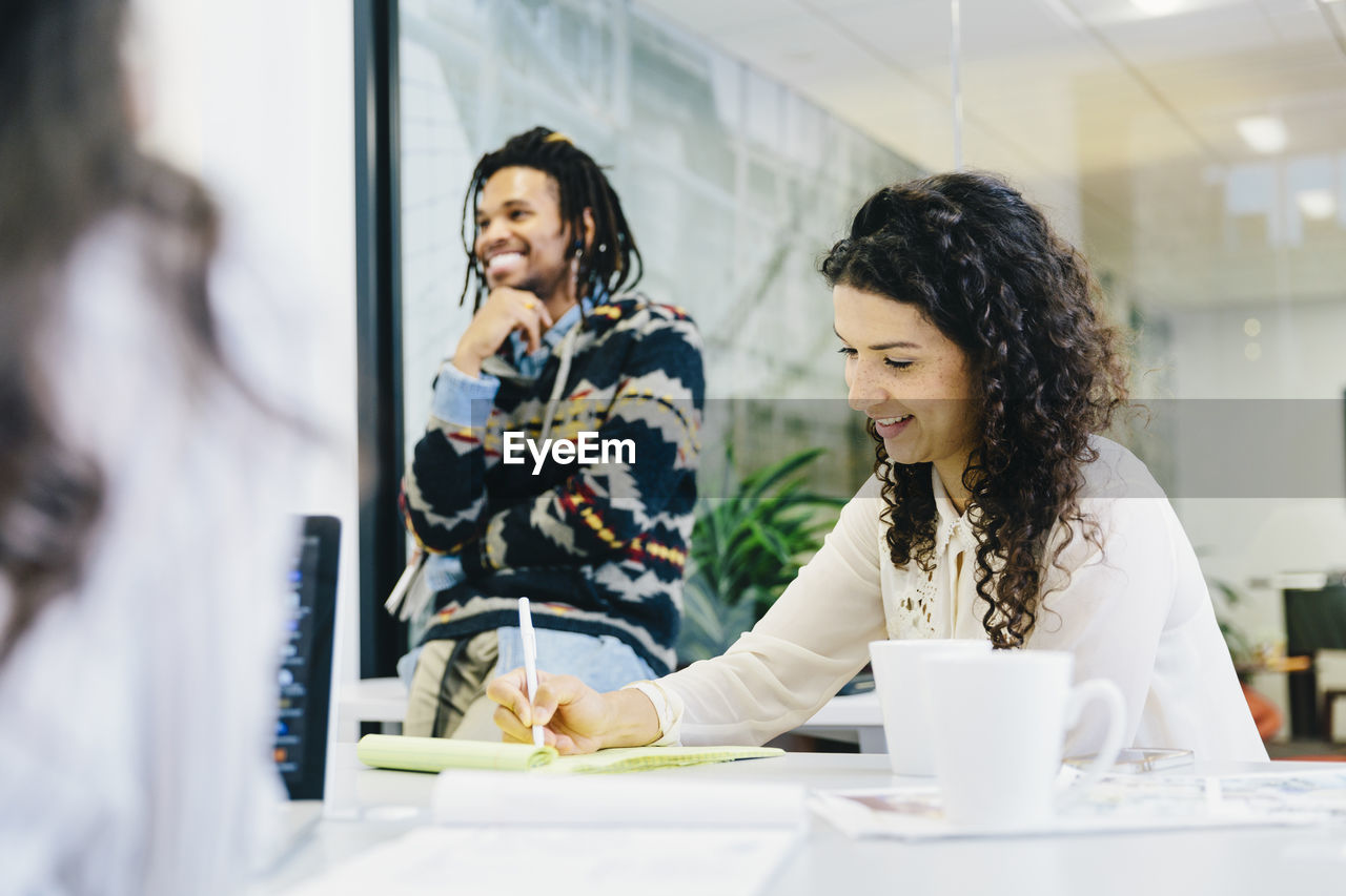 Businesswoman writing on note pad while working with colleagues in conference room