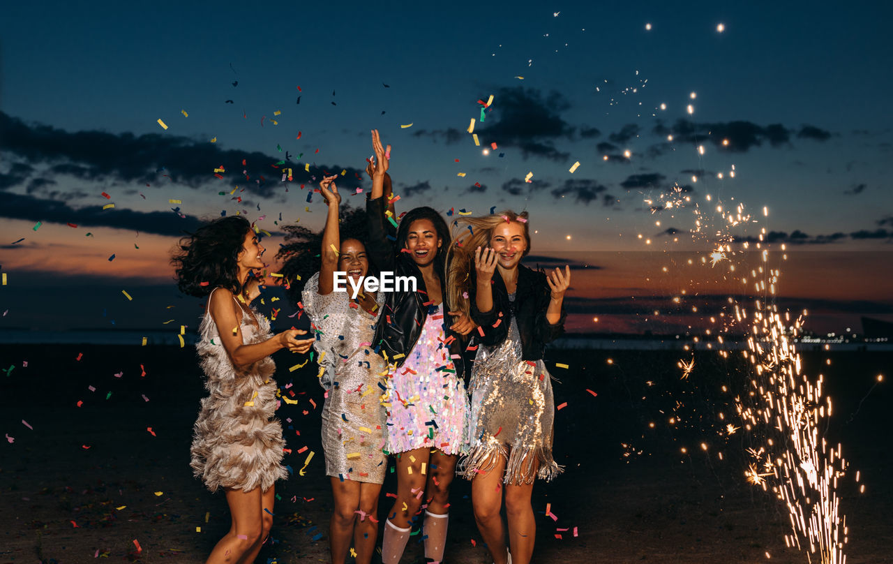 Cheerful female friends partying at beach during sunset