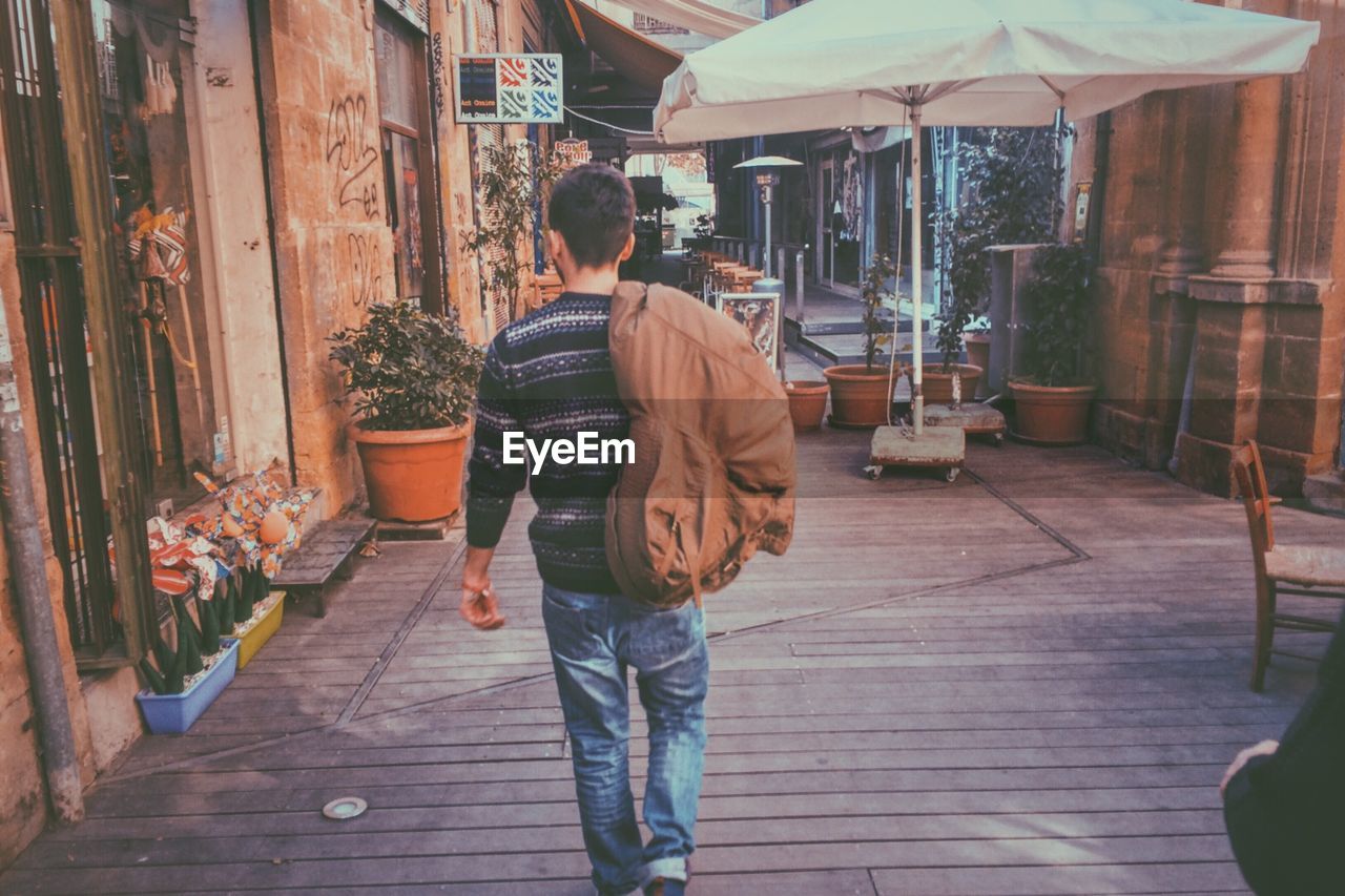 REAR VIEW OF PEOPLE WALKING ON COBBLESTONE