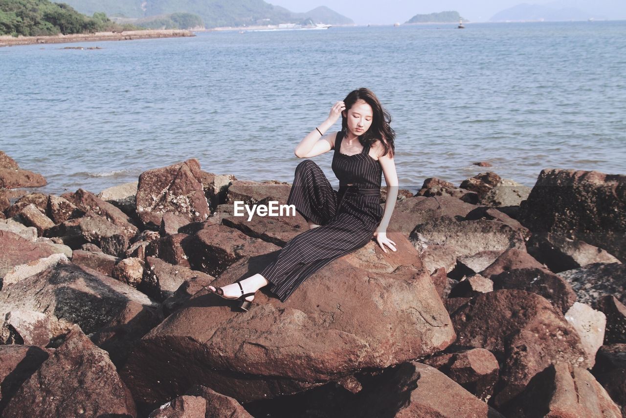 Beautiful fashion model sitting on rocks against sea