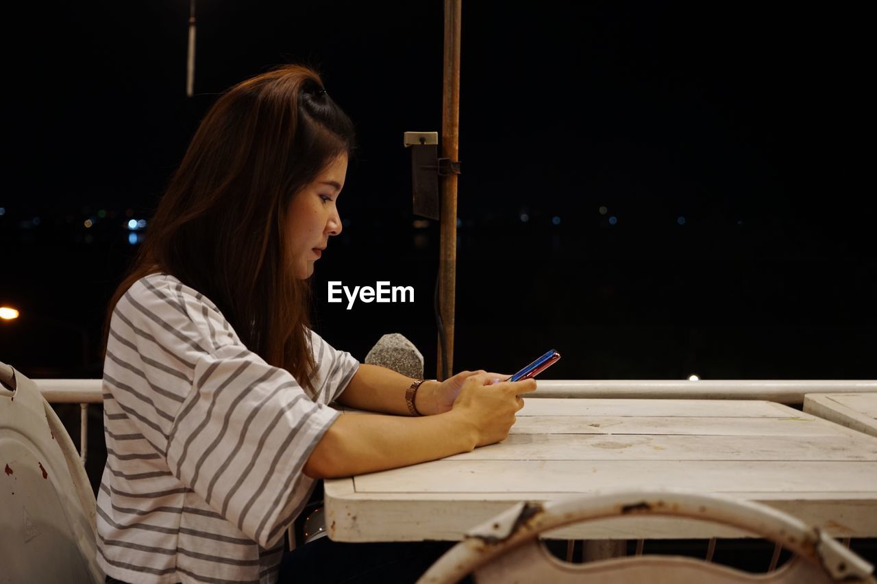 Side view young woman using phone while sitting on restaurant table