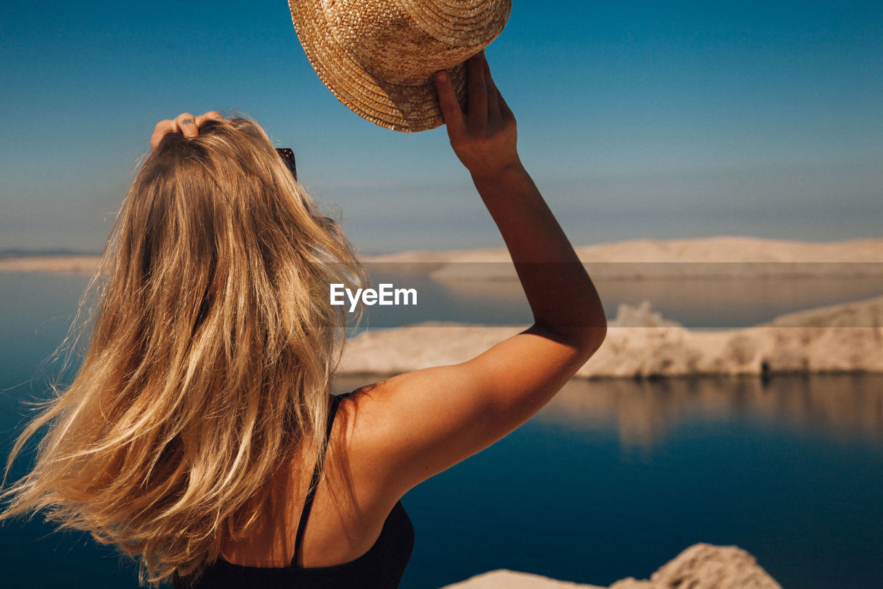 REAR VIEW OF WOMAN WITH HAT IN SEA AGAINST SKY