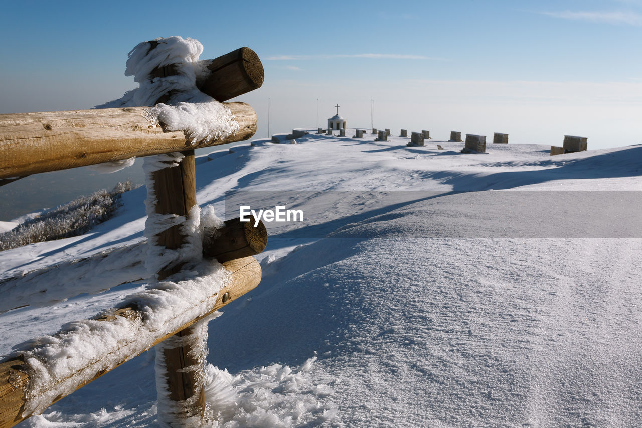 SNOW COVERED WOODEN POSTS ON LAND AGAINST SKY