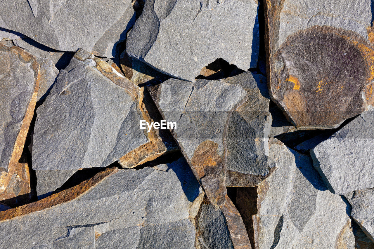 Texture of layered pieces of yellow sandstone stone in harsh sunlight separated by stripes.