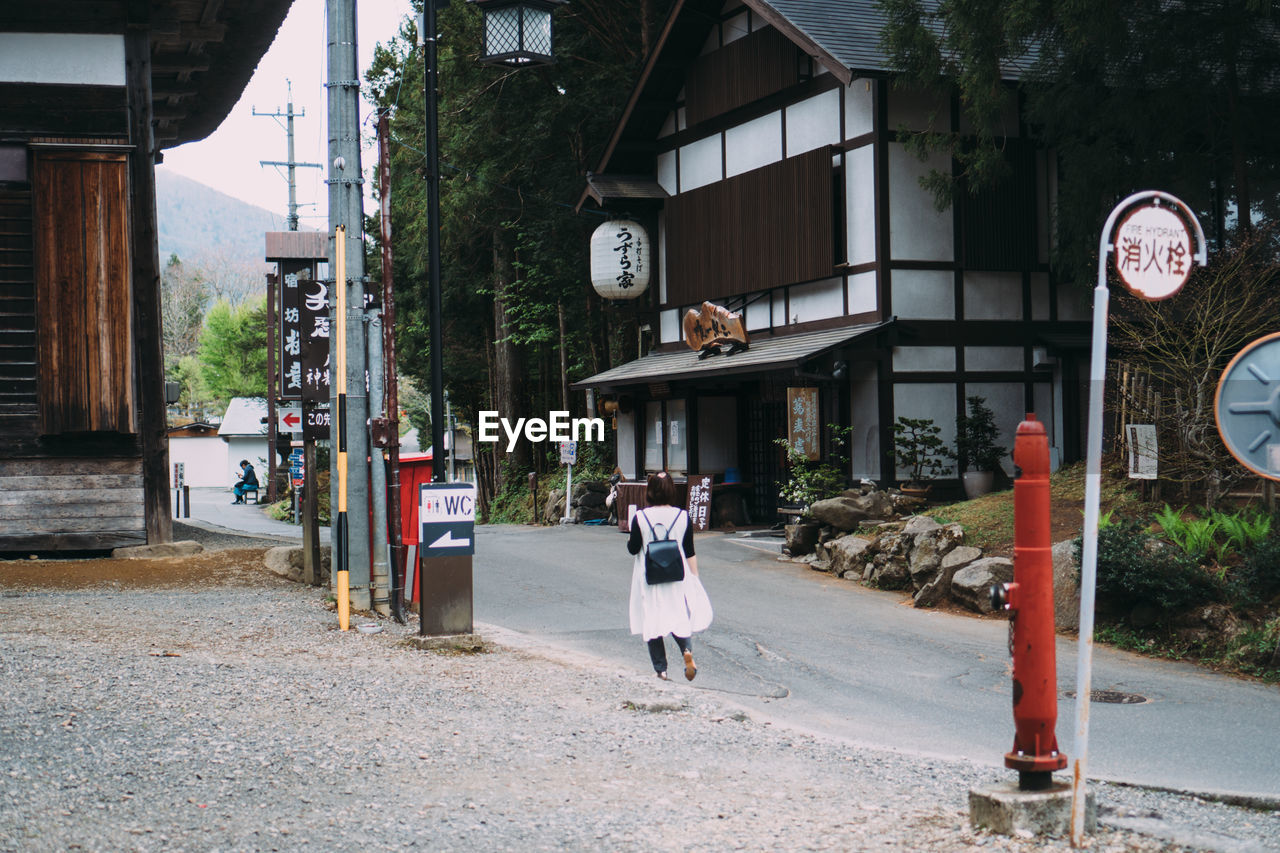 REAR VIEW OF PEOPLE WALKING ON STREET BY BUILDINGS