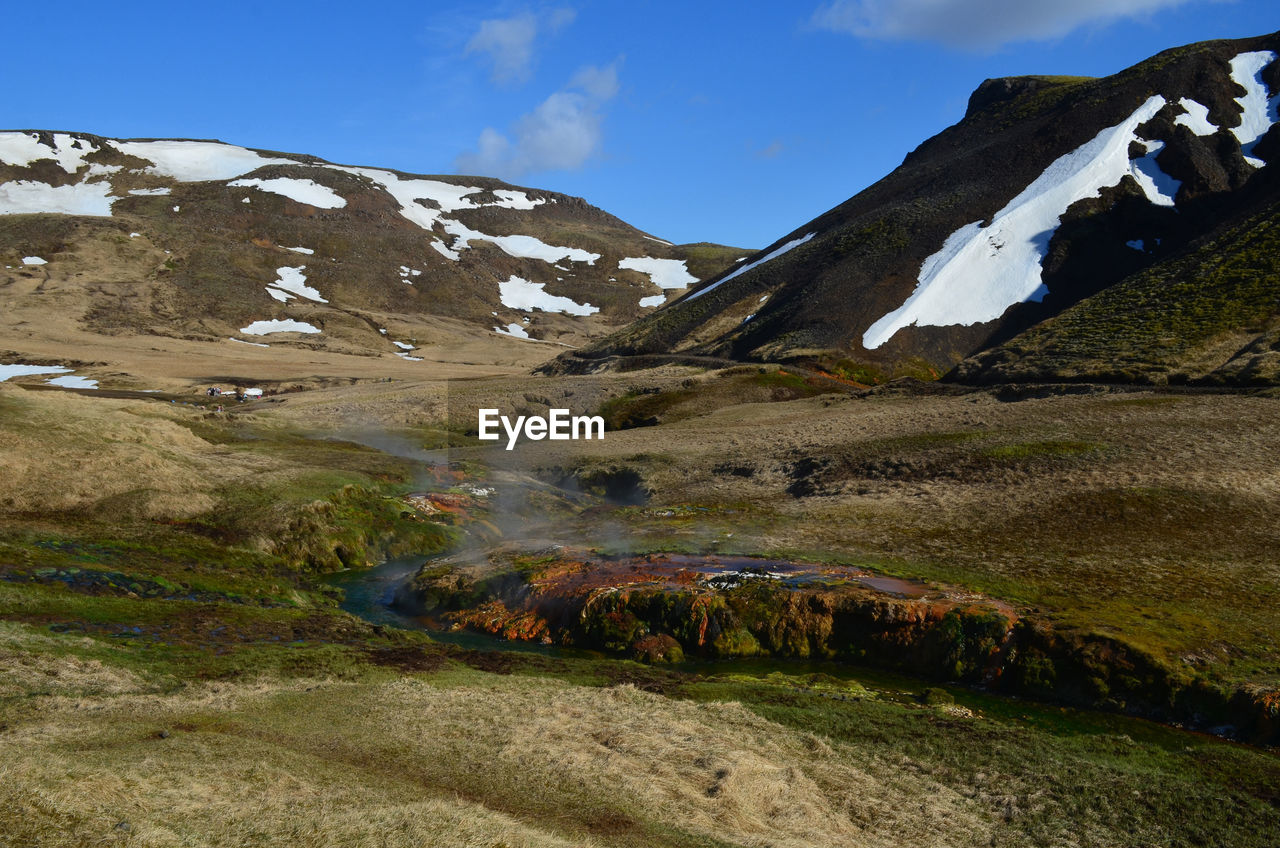 Valley with steam rising from a flowing hot spring in rural iceland.