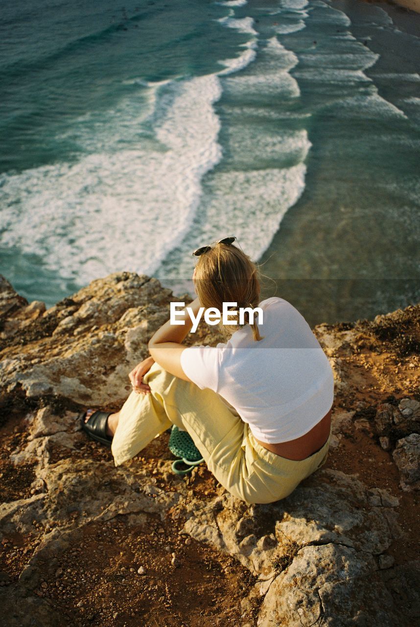 Rear view of woman sitting on rock by sea