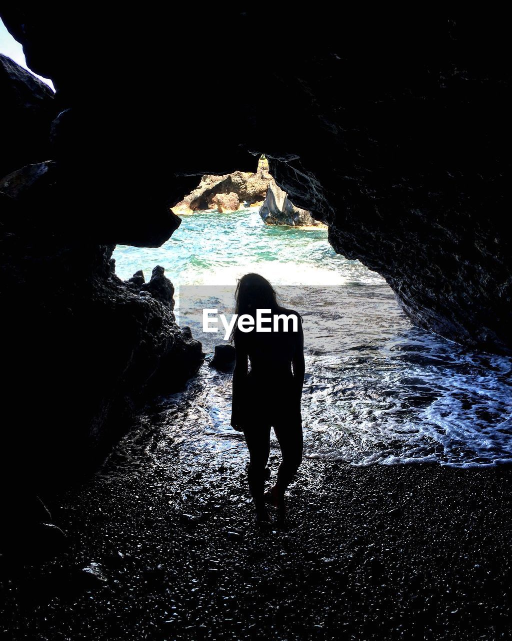 Silhouette of woman standing amidst rock at beach