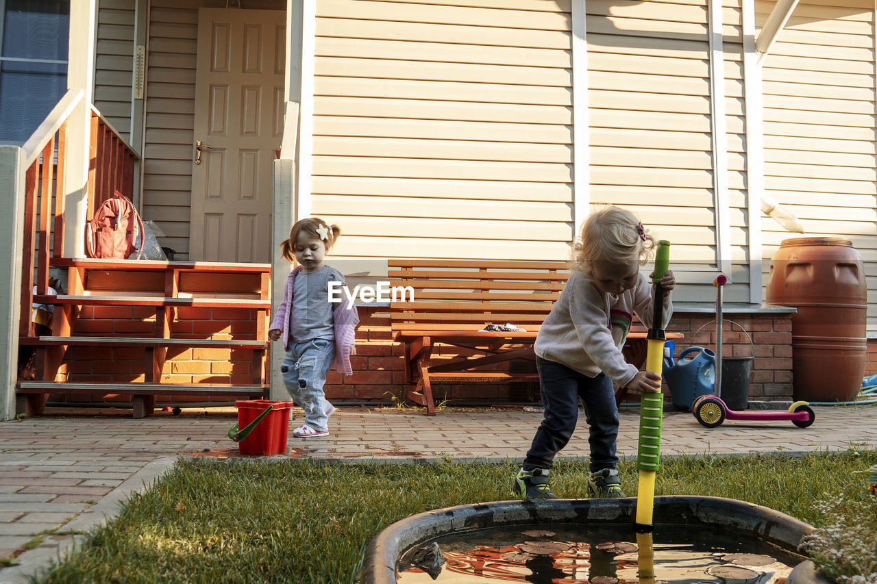 Children playing in the garden with water pump near a small pond.