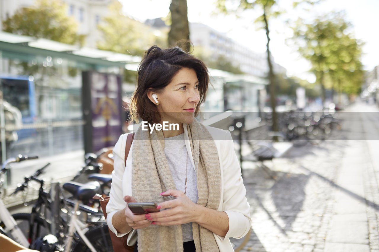 Smiling businesswoman using smart phone and earphones