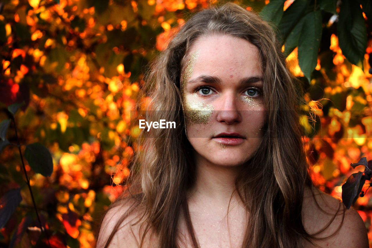 Close-up portrait of young woman with glitter make-up by trees