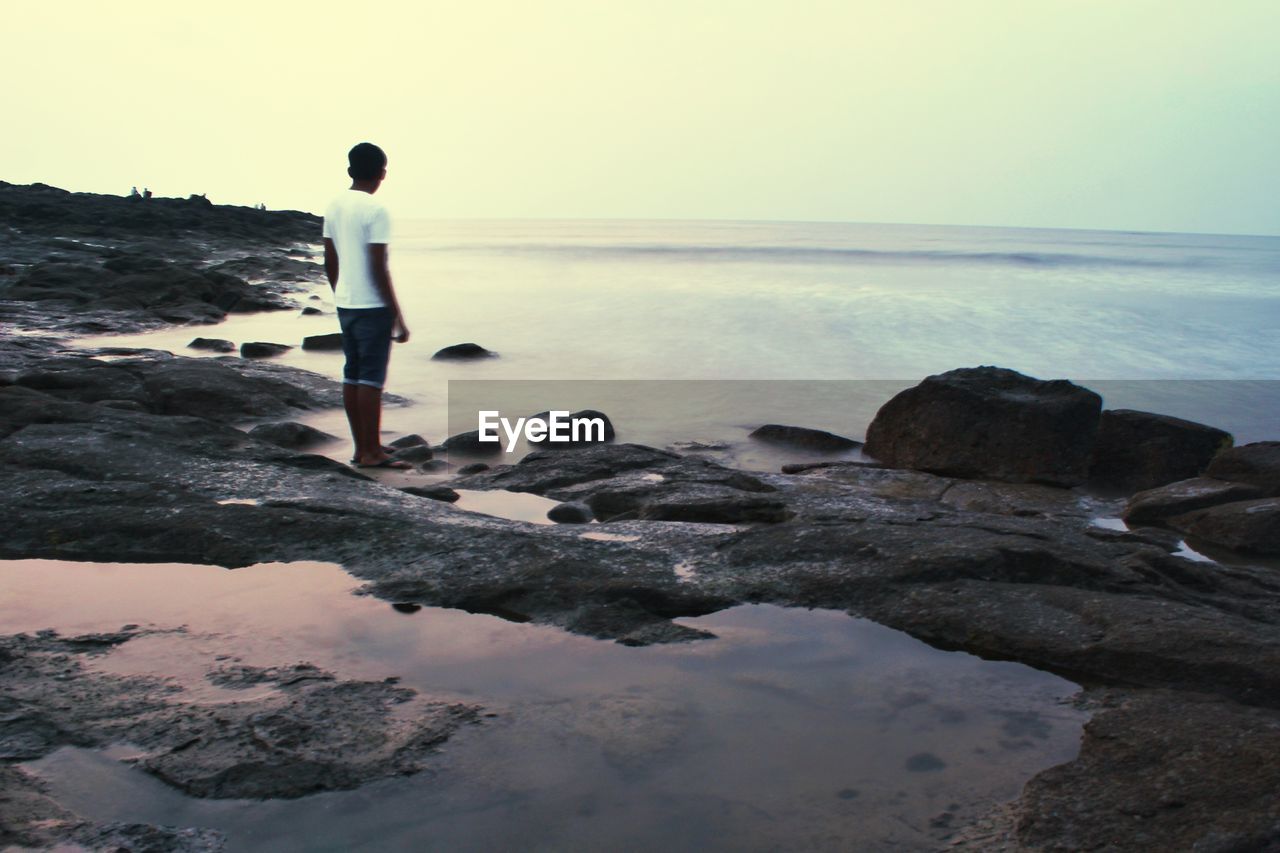 FULL LENGTH OF MAN STANDING ON ROCK AT BEACH