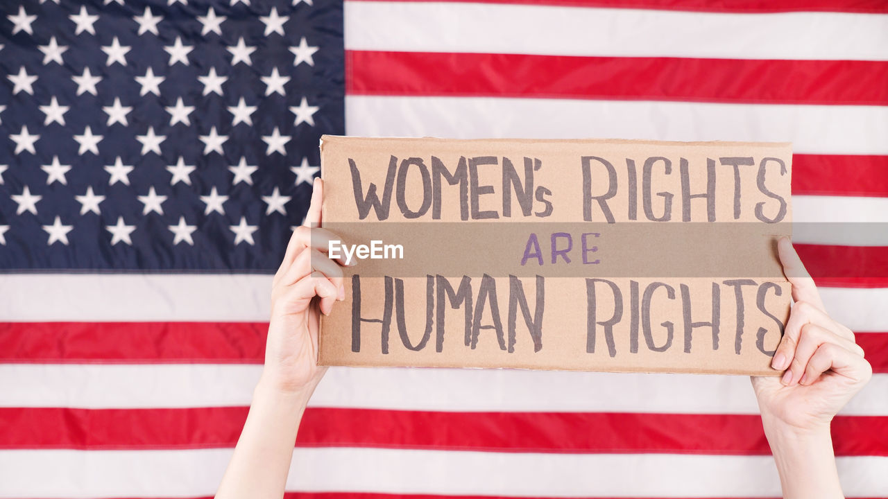 Young woman protester holds cardboard wonen rights are human rights against us flag