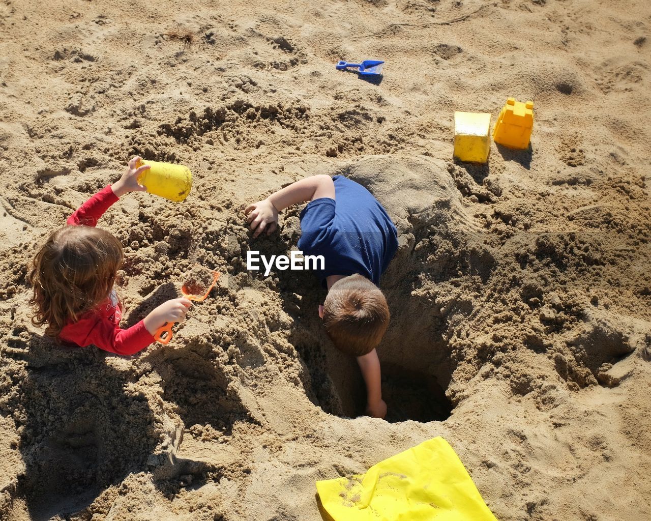 High angle view of playful siblings digging at beach