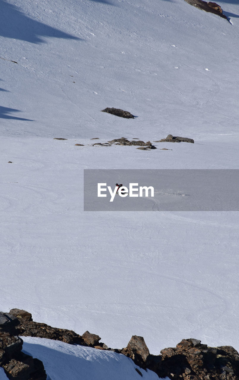 snow, cold temperature, winter, mountain, leisure activity, winter sports, adventure, sports, nature, skiing, environment, landscape, day, scenics - nature, beauty in nature, extreme sports, travel, vacation, travel destinations, mountain range, land, trip, holiday, outdoors, full length, non-urban scene, high angle view, lifestyles, piste, frozen, water, one person, tourism, recreation, activity, snowcapped mountain, snowboarding, rock, ski equipment, men