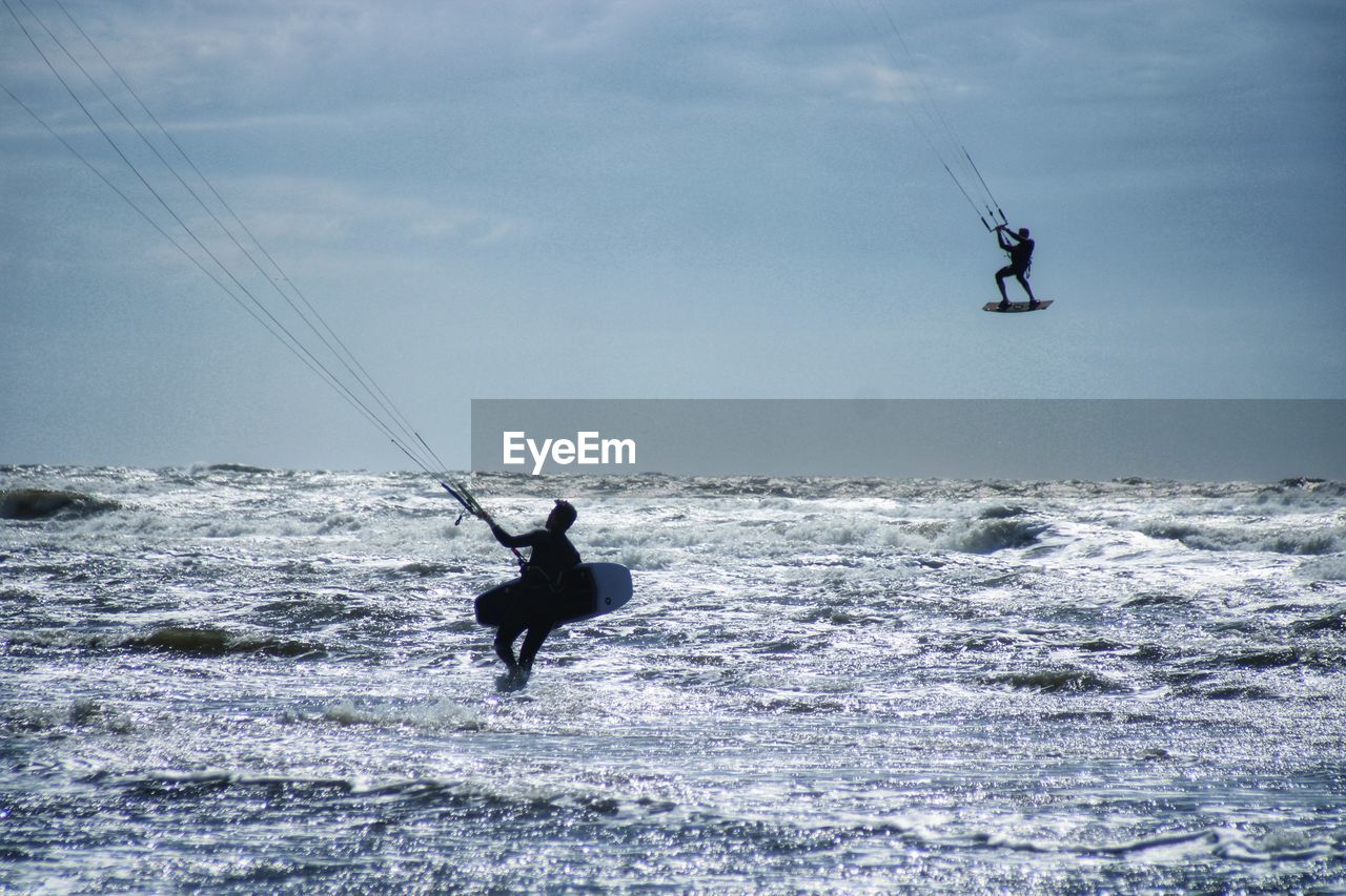 Men surfing in sea against sky