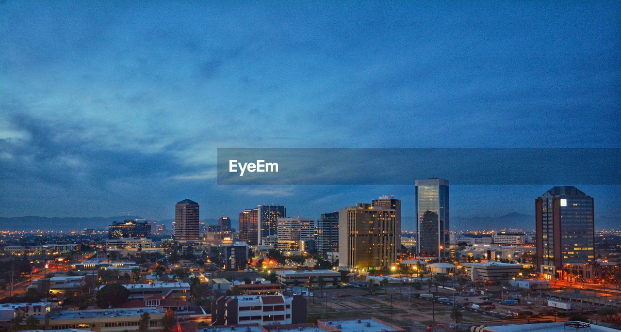 Illuminated buildings in city against sky at dusk