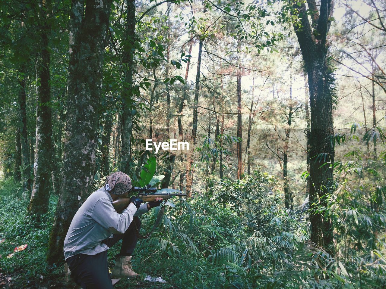 Man aiming rifle while crouching in forest