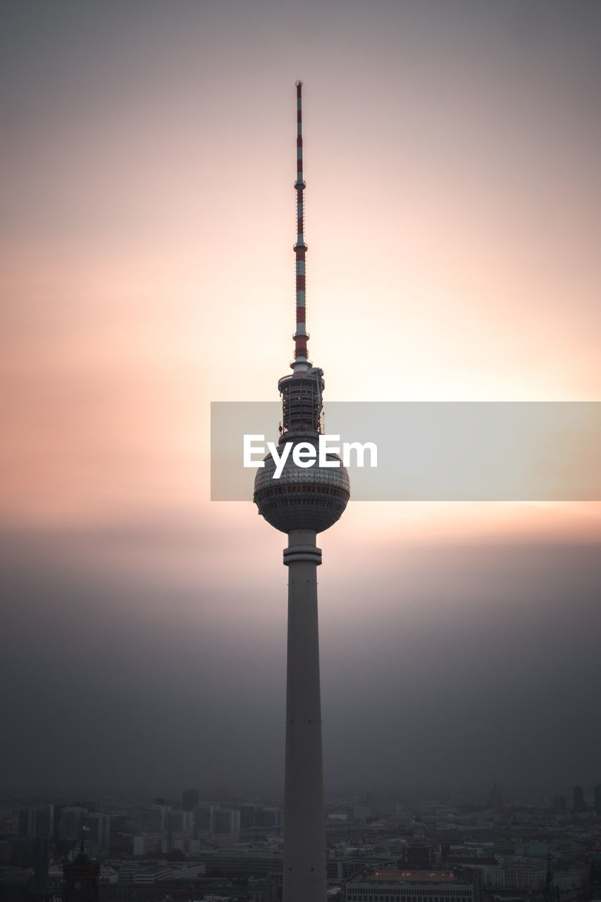 Communications tower in city against romantic sky at sunset