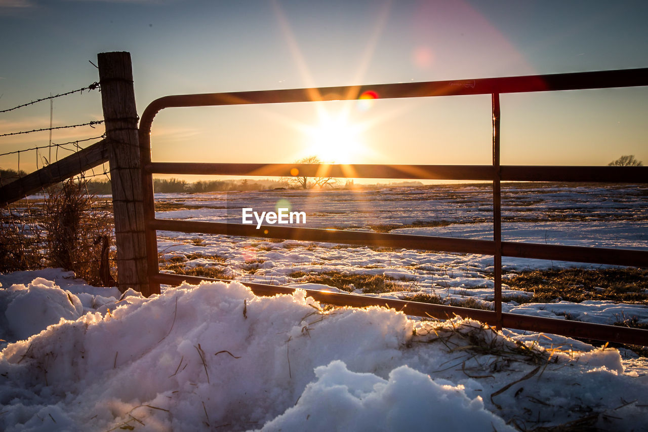 Fence on snow covered field during sunset