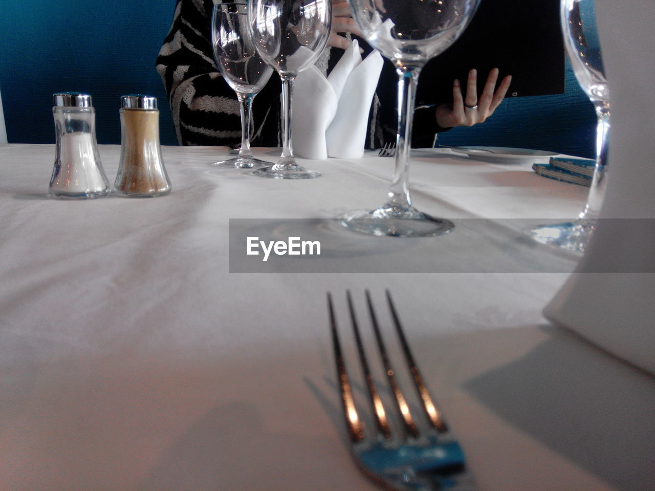 Midsection of person sitting by table with salt and pepper shakers at restaurant