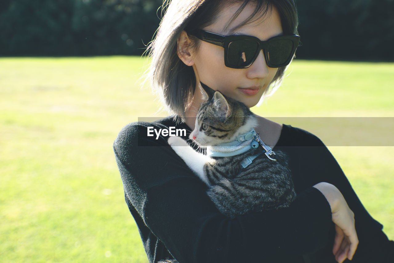 Woman wearing sunglasses while holding cat on field