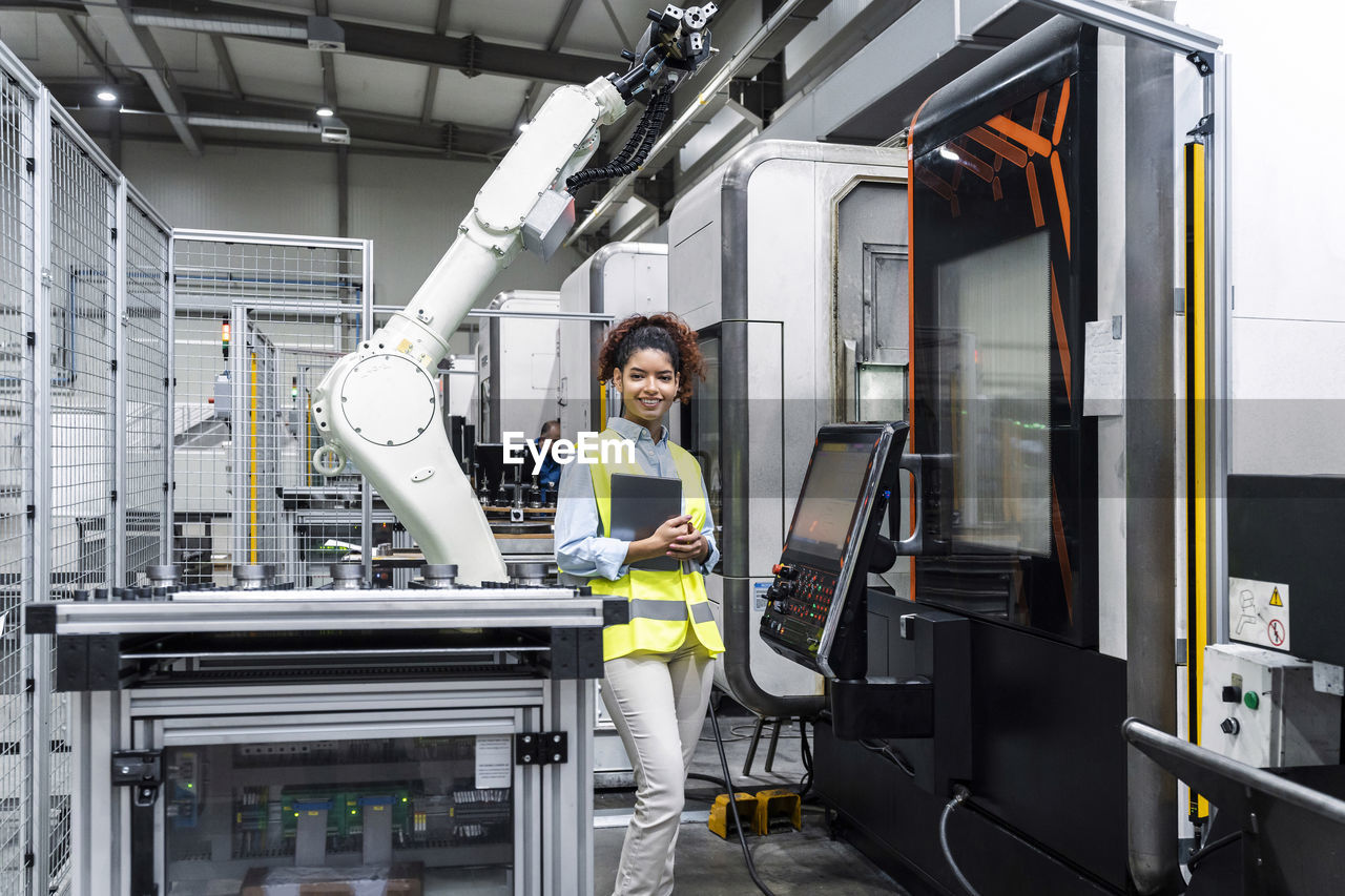 Smiling engineer standing with tablet computer by machine in factory