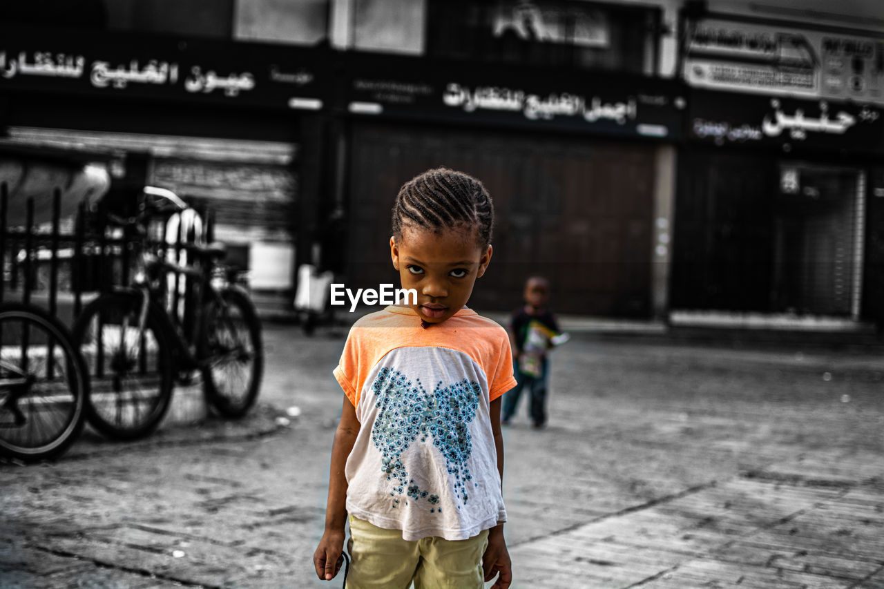 FULL LENGTH PORTRAIT OF BOY STANDING ON STREET IN CITY