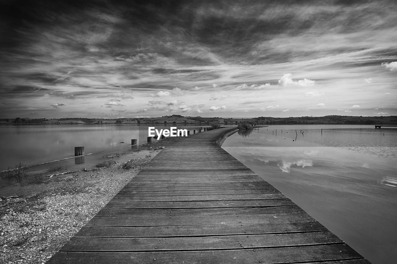 Wooden pier leading towards sea against sky