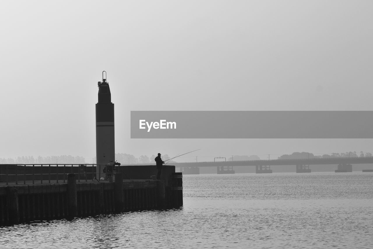 Man fishing by lighthouse against clear sky