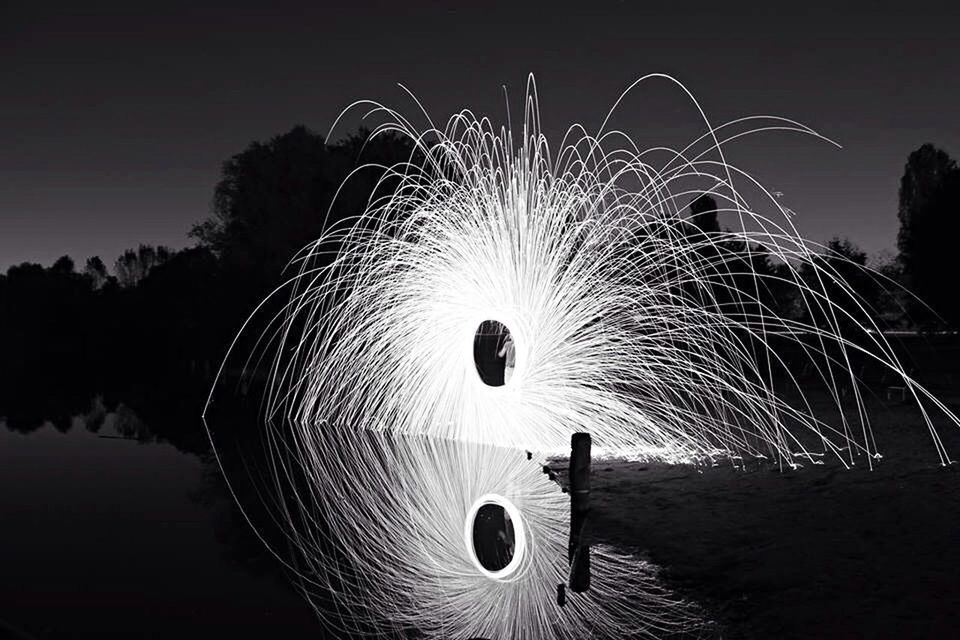 Light painting by river with trees against sky