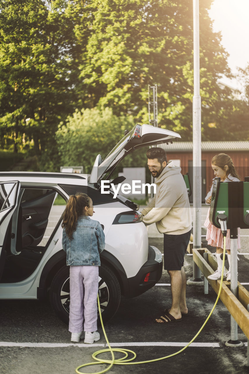 Father talking to daughter charging electric car at station