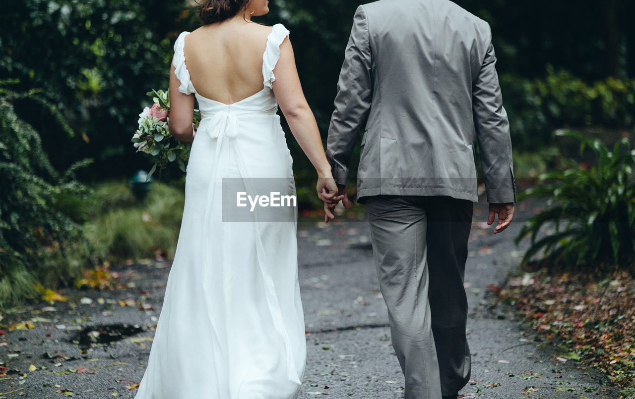 Rear view of newlywed couple holding hands while walking on footpath