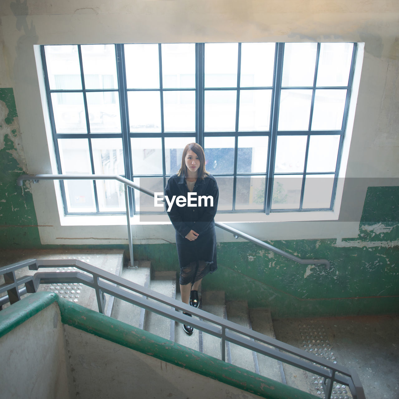 Portrait of young woman standing on steps against window