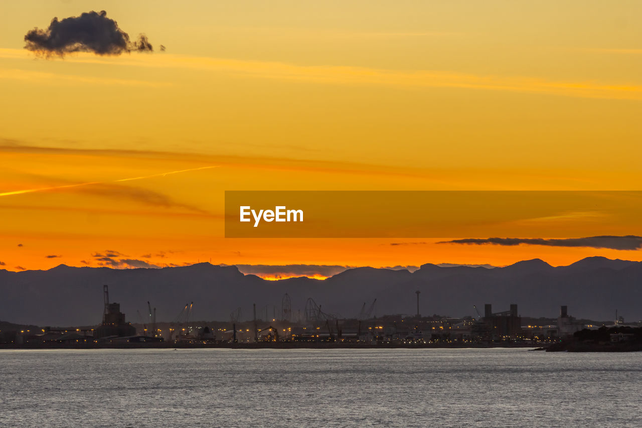 SEA BY SILHOUETTE MOUNTAINS AGAINST ORANGE SKY