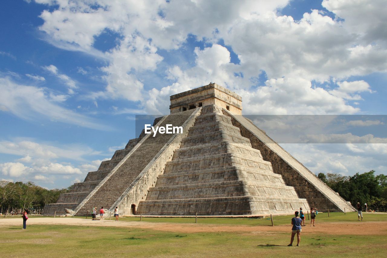 People at kukulkan pyramid of chichen itza against sky