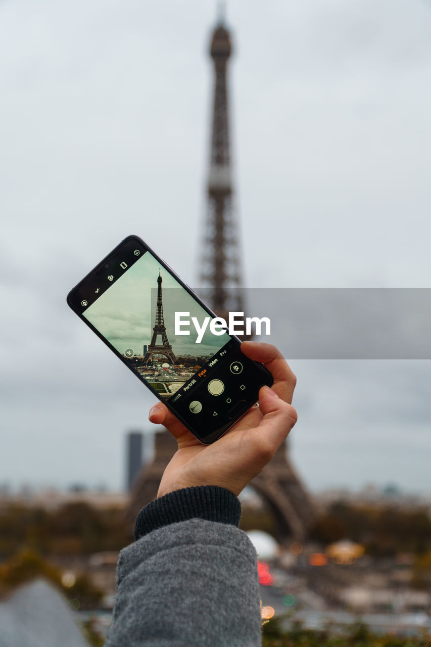 Midsection of person holding smartphone to take from eifel tower in paris