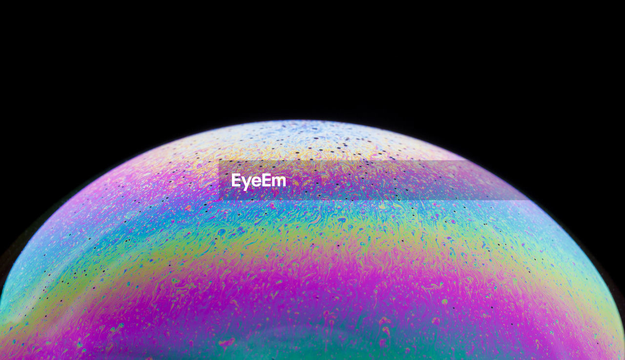 Panoramic view of closeup bubble textured backdrop representing colorful planet with wavy lines on round shaped surface on black background