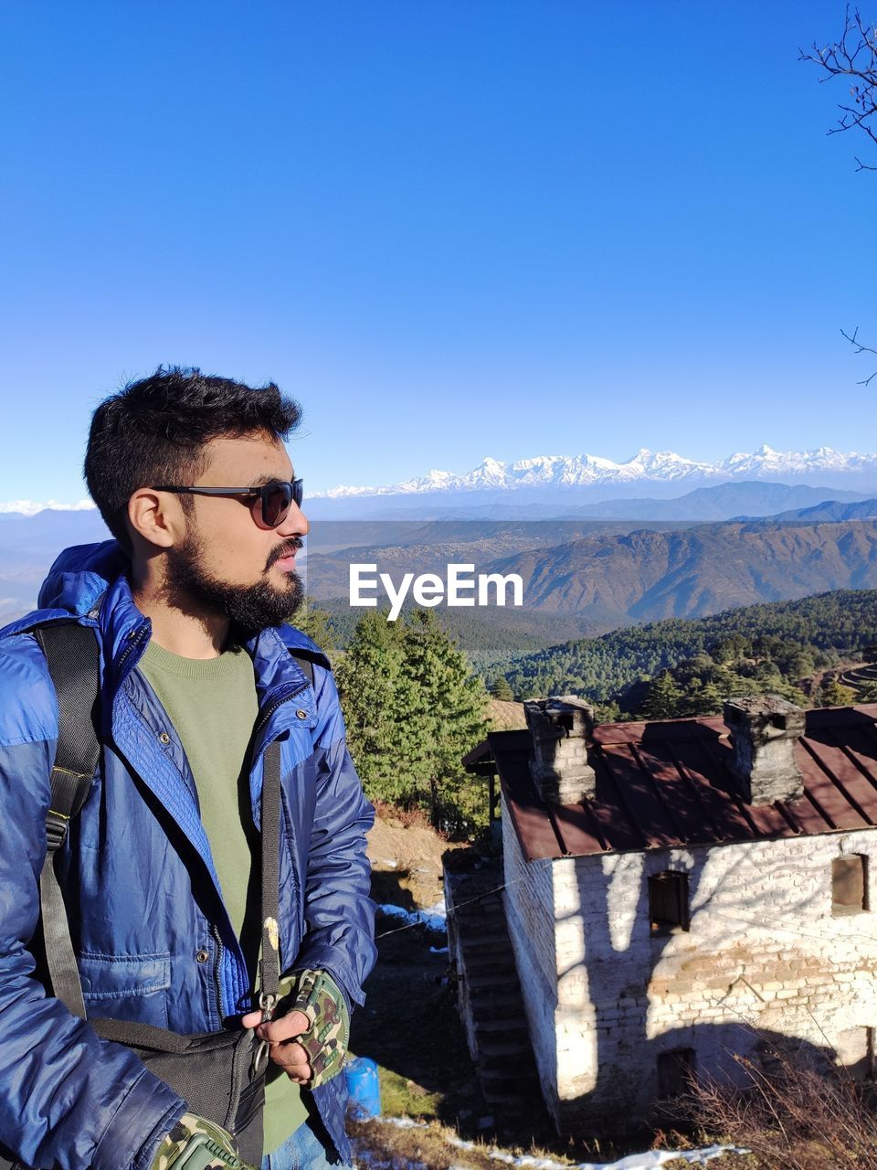 Young man standing against mountain range against clear blue sky