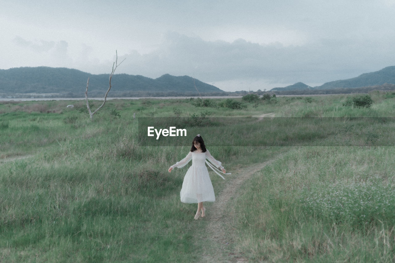 REAR VIEW OF WOMAN STANDING ON FIELD BY LAND