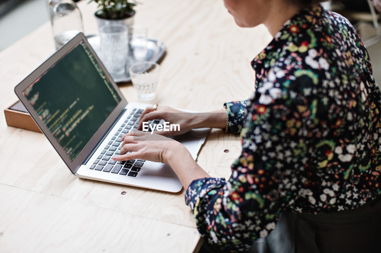 Midsection of businesswoman using laptop at table in office