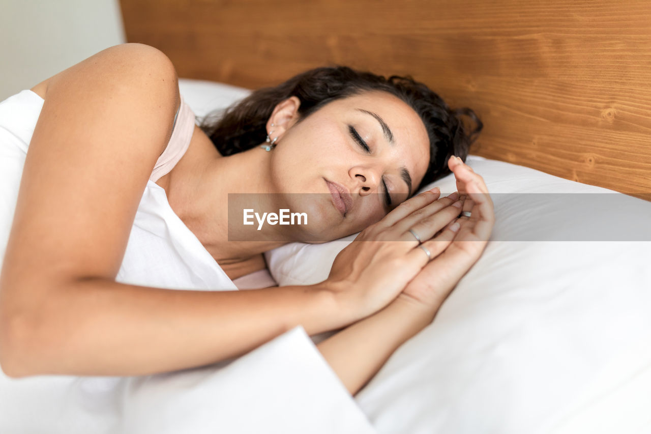 Calm female in pajama lying in bed on soft pillow under white blanket and sweetly sleeping